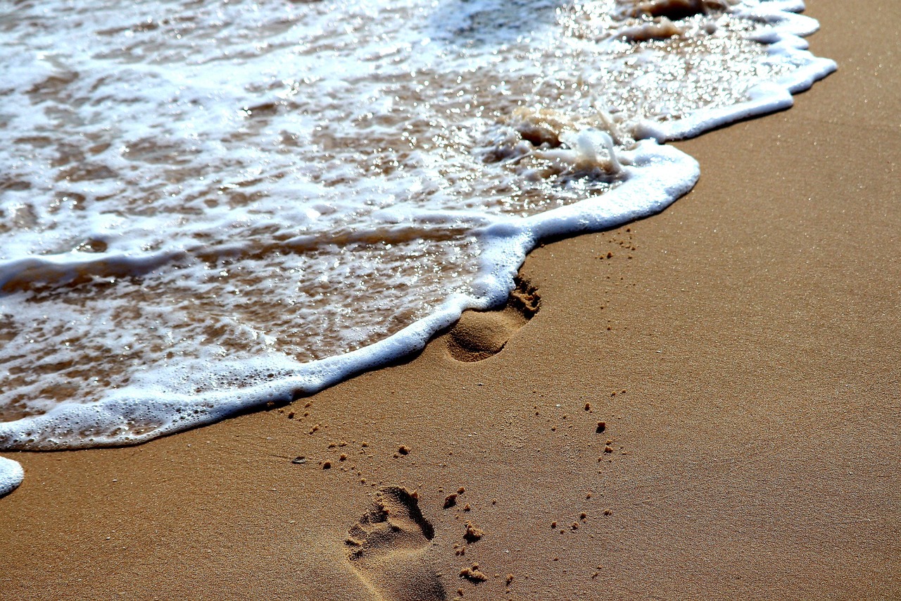 Fußspuren im Sand werden von einer Welle überspült. Foto: Thomas G., Pixabay